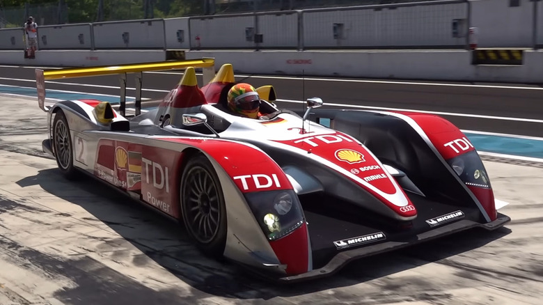 A silver and Red Audi R10 LMP1 Le Mans race car with stickers showing that its TDI diesel powered on a track.