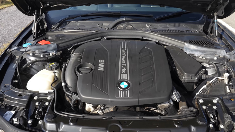 The engine bay of a black BMW 335d from the early 2010s open, showing the engine inside.