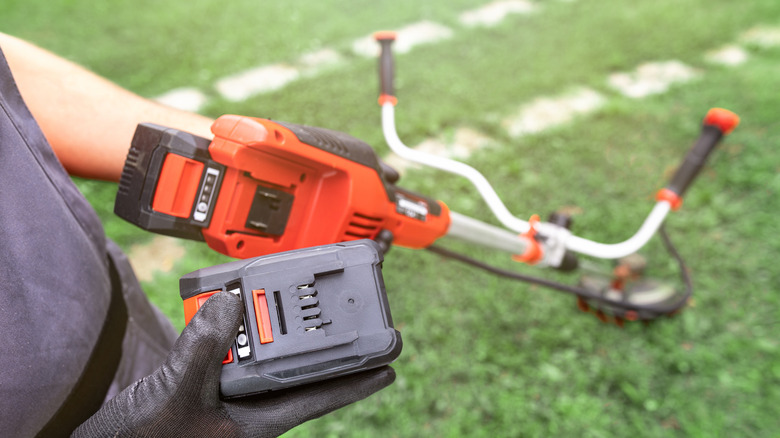 Person holding electric weed trimmer battery.