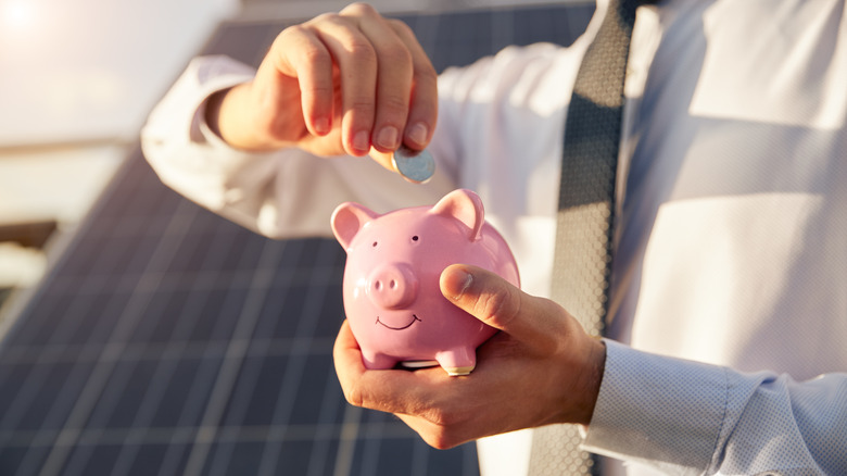 A person putting coins into a pink piggy bank with a solar panel visible behind them