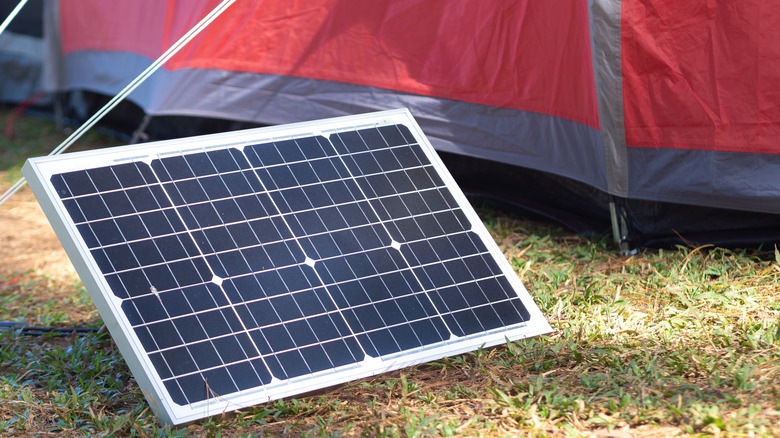 A portable solar panel sitting on grass next to a red tent
