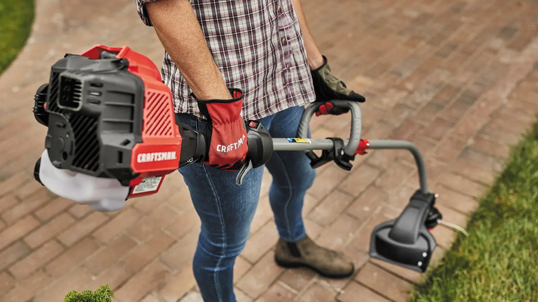 A man trimming the edge of a pathway with a gas-powered Craftsman string trimmer