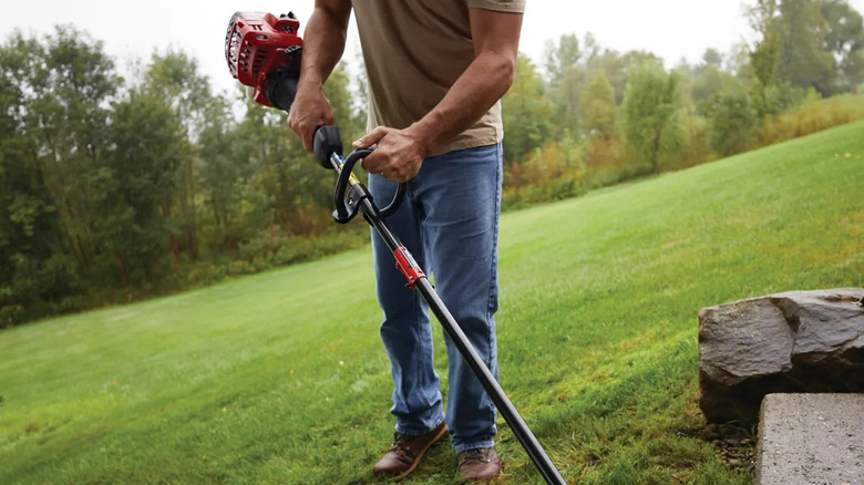 A man trimming his lawn with a gas-powered Craftsman weed eater