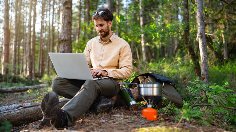 Person using laptop while sitting in the woods outdoors.