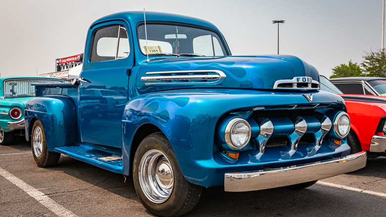 A classic bright blue Ford pickup truck parked in a lot with other classic cars