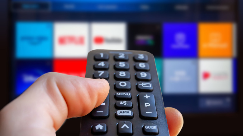 hand holding remote control, blurred background of a TV with streaming services