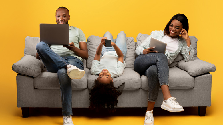 A family sitting on the couch using electronic devices
