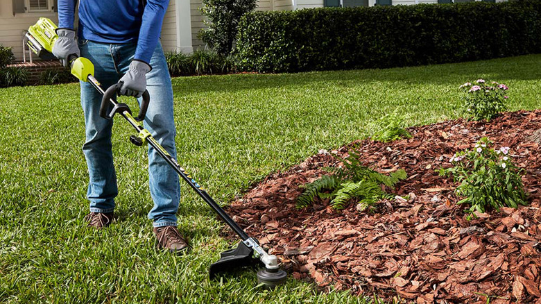 A person trimming the edge of a lawn with a string trimmer