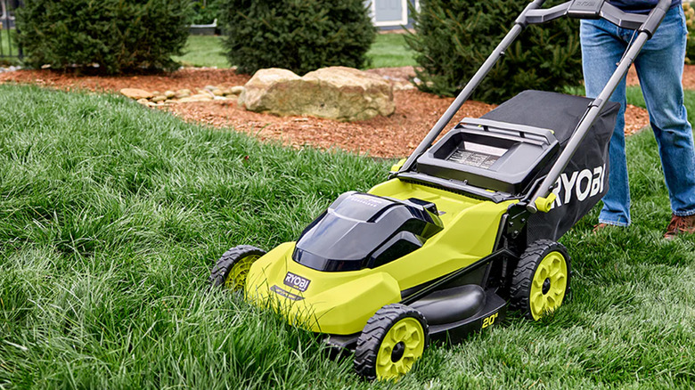 A person mowing long grass with a Ryobi lawnmower