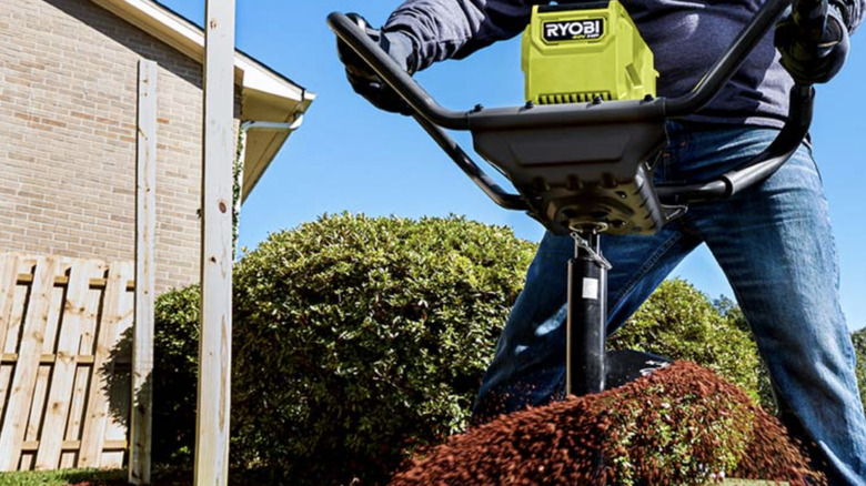 A man in blue jeans and work gloves using a Ryobi earth auger