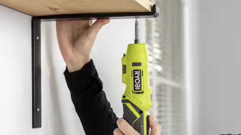 A close-up of a person using a small Ryobi screwdriver to install a shelf