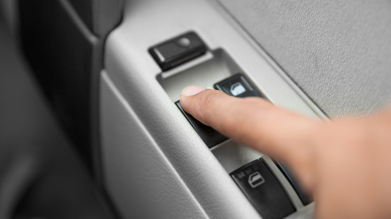 Close-up of hand pressing button to operate car power window.