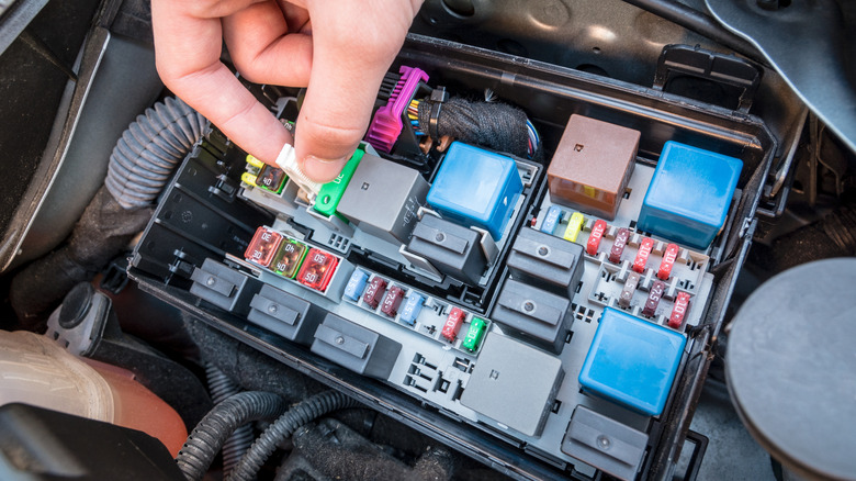 Close-up of hand checking fuse box in modern car engine.