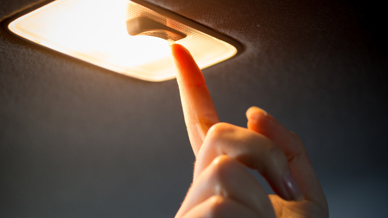 Close-up of hand turning on car interior dome light.