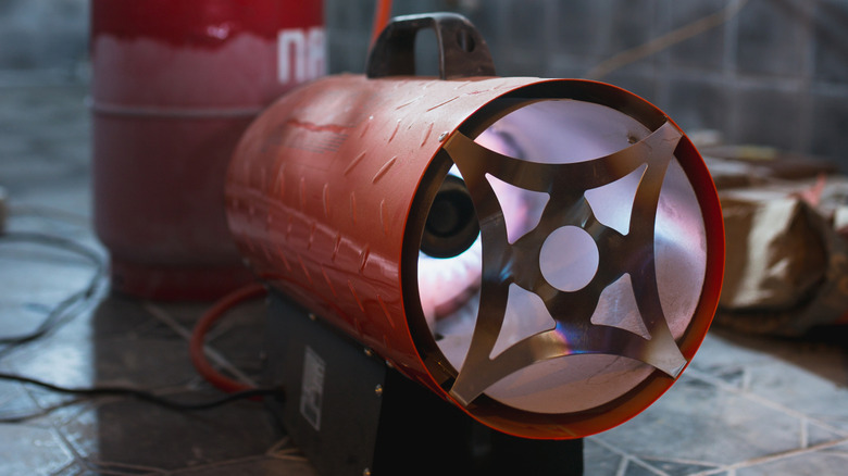A blower heater on the ground in front of a propane tank.