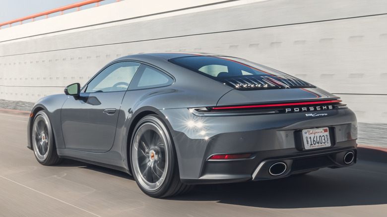 Rear 3/4 view of grey Porsche 911 Carrera Coupe on road with wall in background