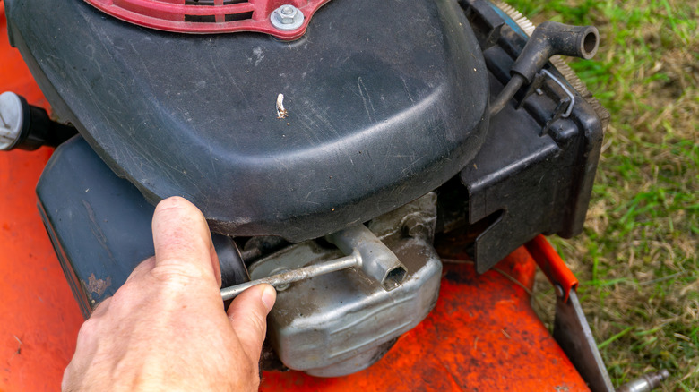 A person using a tool on a lawn mower.