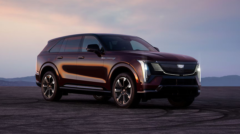 A purple 2026 Cadillac Escalade full-size, all-electric SUV parked with its lights on off a paved road.