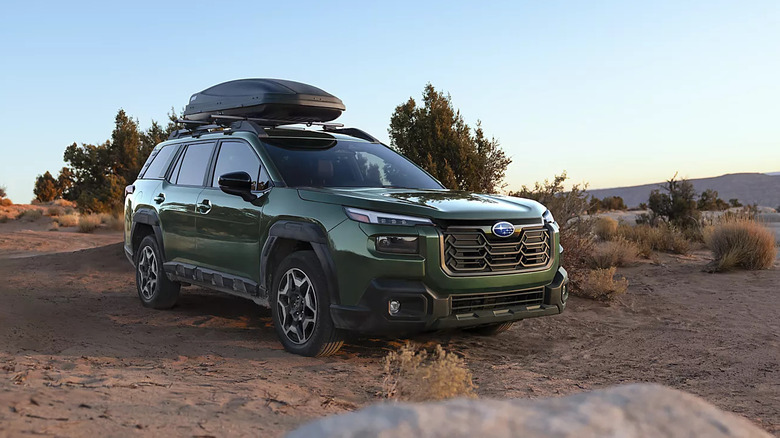 A dark green 2026 Subaru Outback standing off road with a roof box in the evening, right three-quarter view shown.