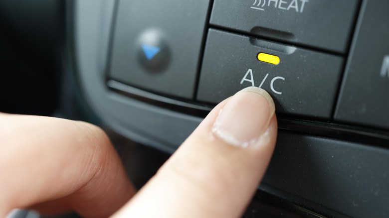 A person pressing a button to enable air conditioning in a vehicle