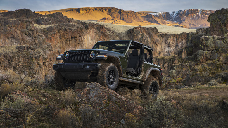 A 2024 Jeep Wrangler Willys without a top or doors parked on a rock in the desert