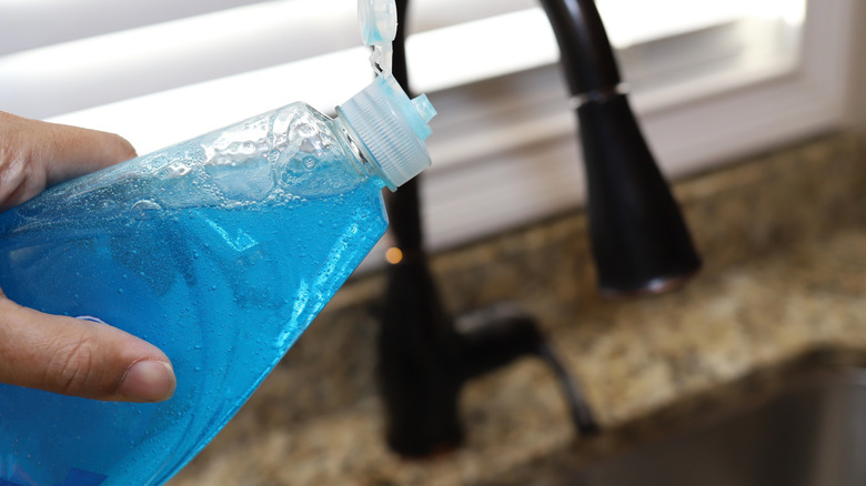 A woman holding a bottle of dish detergent in her hand.