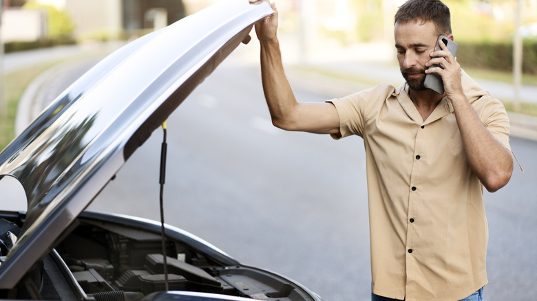 A sad driver opening the hood of their car and talking on the phone.