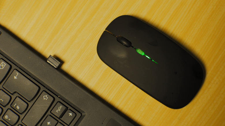 A wireless mouse next to a laptop with its dongle plugged into the USB port
