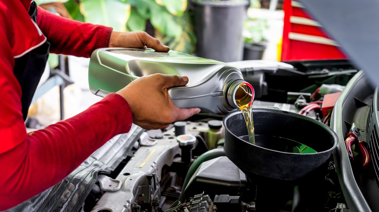 A person in a red and black shirt pouring oil into a vehicle using a large funnel