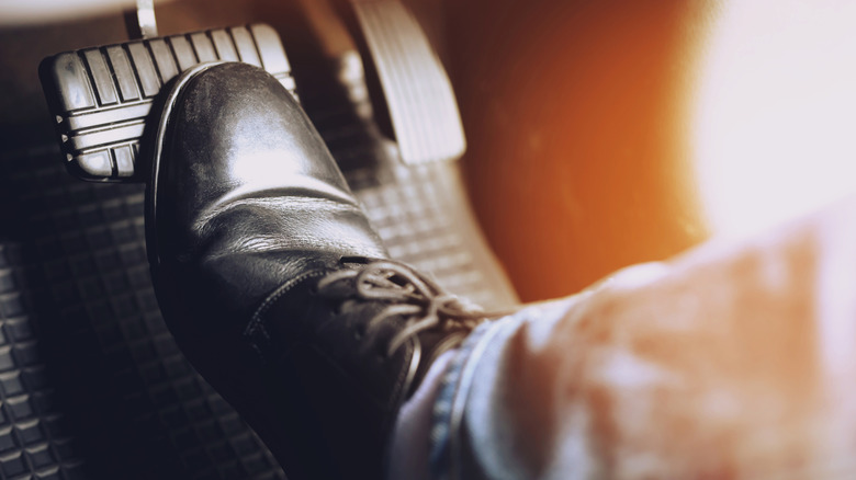 Close-up of a man's foot in a black shoe stepping on the brake pedal of a vehicle