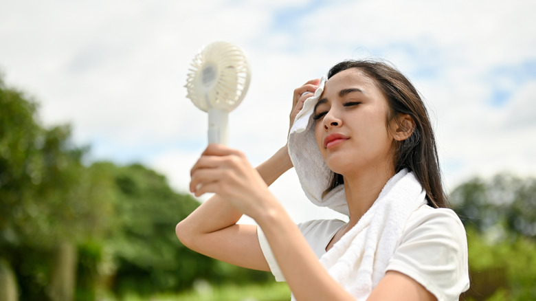 Woman wiping sweat and using handheld fan while outdoors