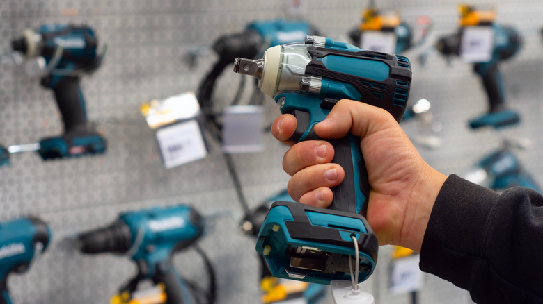 A person holding a teal power drill in front of a hardware store display with various tools