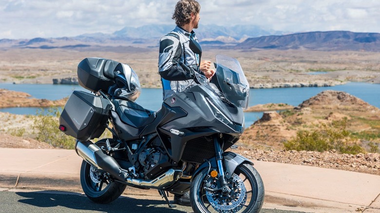 Man standing beside Honda touring motorcycle and looking at lake.