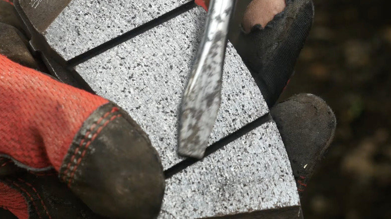 Gloved hand holds flat head screwdriver on brake pad with uneven wear