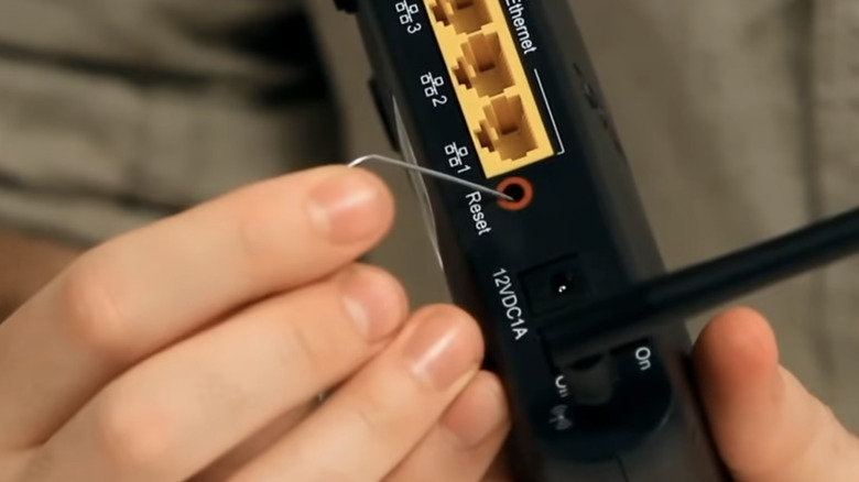 Hand pushes the reset button on a router with a pin