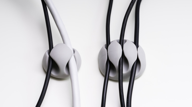 Grey cord organizers stuck to the wall holding black and white cables