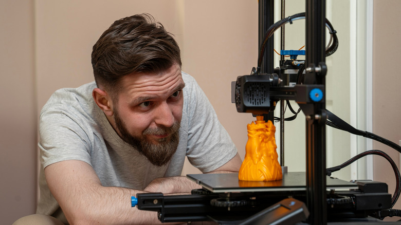 A casually-dressed man watching a 3D printer at his home
