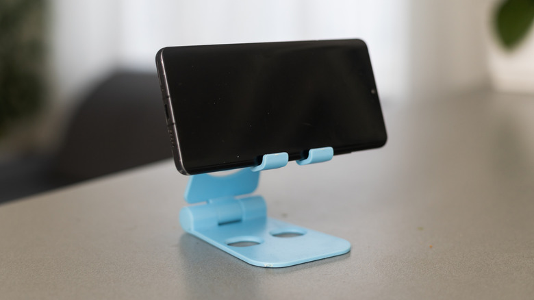 A smart phone sitting horizontally in a blue mobile phone holder on top of a table