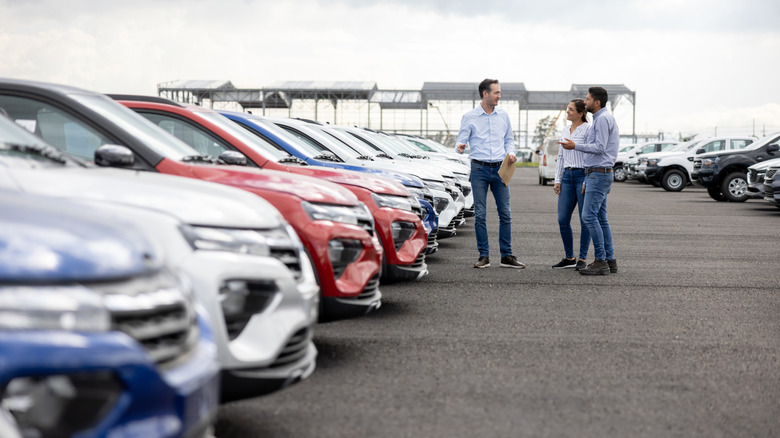 Couple at car dealership with a sales representative, out of focus cars in the foreground