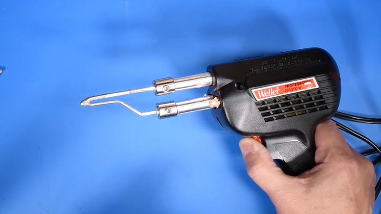 A person demonstrating the Weller soldering gun against a blue background