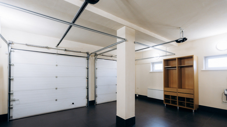 A clean garage space with two closed garage doors and empty shelving with no clear form of lighting installed