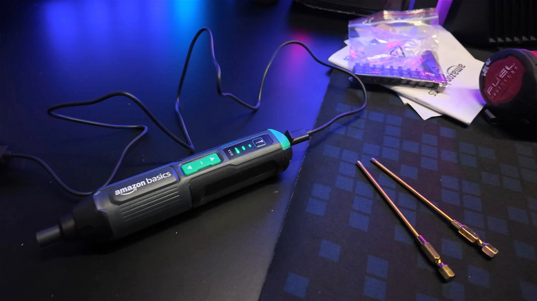 An Amazon Basics electric screwdriver in charge on a desk next to other tools.