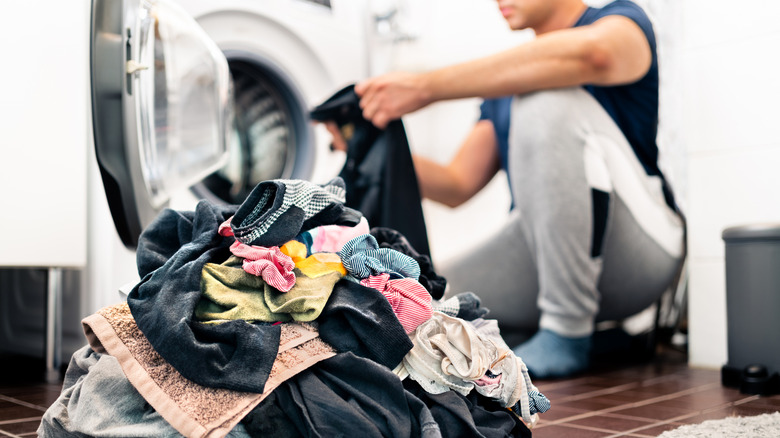 man loading washing machine with pile of dirty clothes