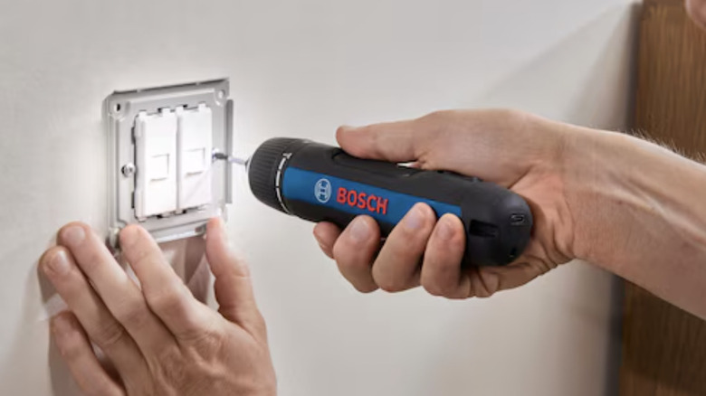 Close-up of someone using a Bosch rechardable screwdriver to install a light switch assembly