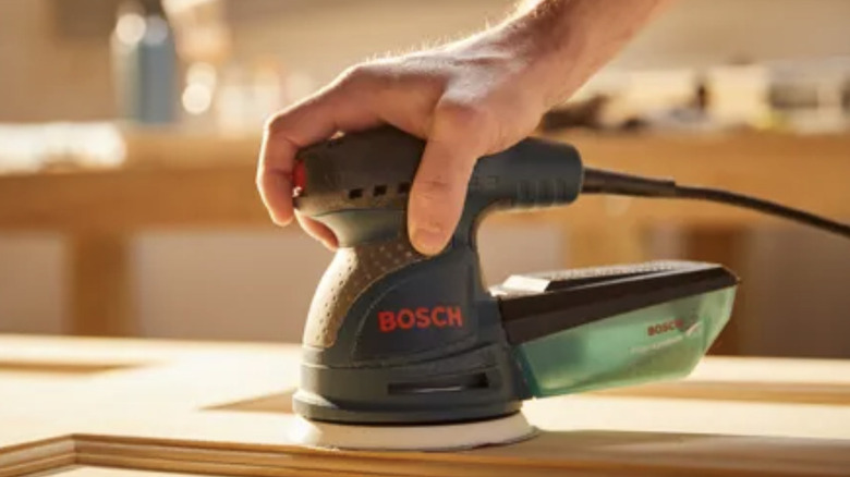 A man using a corded Bosch palm sander on a wood surface