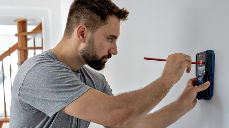 A man using a Bosch wall scanner to mark an area on a white wall