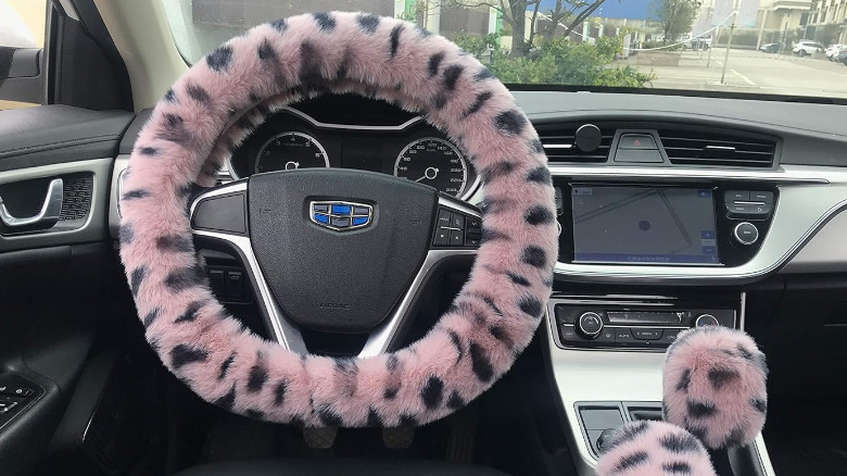 A fluffy pink and black leopard-print steering wheel cover in a car.