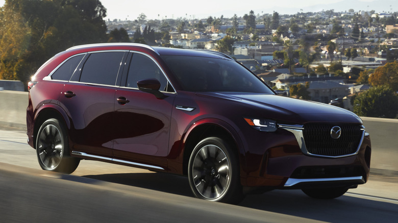 Front 3/4 view of Mazda CX-90 on freeway ramp in suburban setting