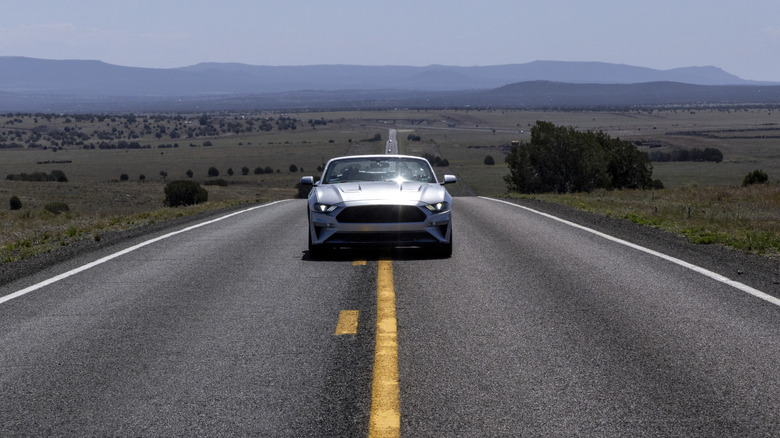 A silver convertible driving down the center of an empty two-lane road in a rural area