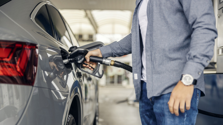 Close up of a man in a grey shirt and blue jeans filling up a modern silver sedan at a fuel pump